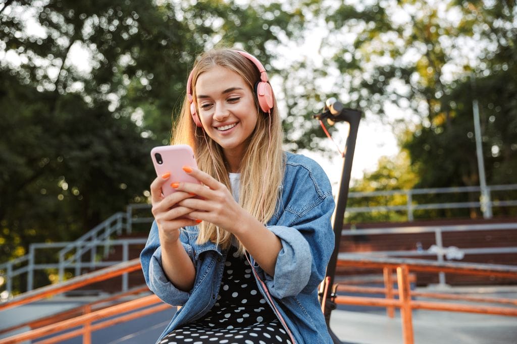 Chica adolescente sonriente con móvil en el exterior