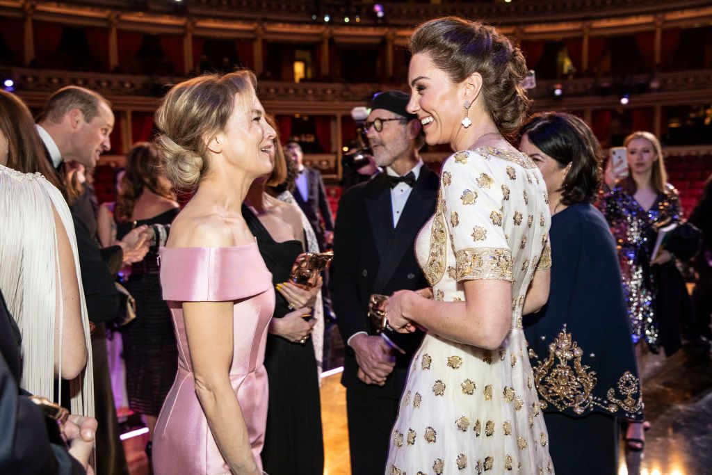 La Princesa Kate con un vestido blanco bordado en oro conversa con Renée Zellweger en los Premios BAFTA, rodeada de celebridades en un elegante auditorio