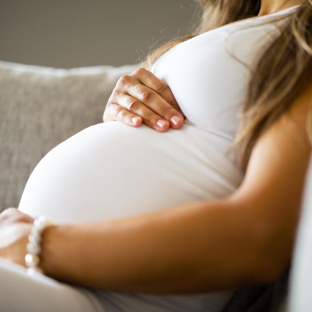 Close-up of pregnant woman sitting in sofa with her hands at belly