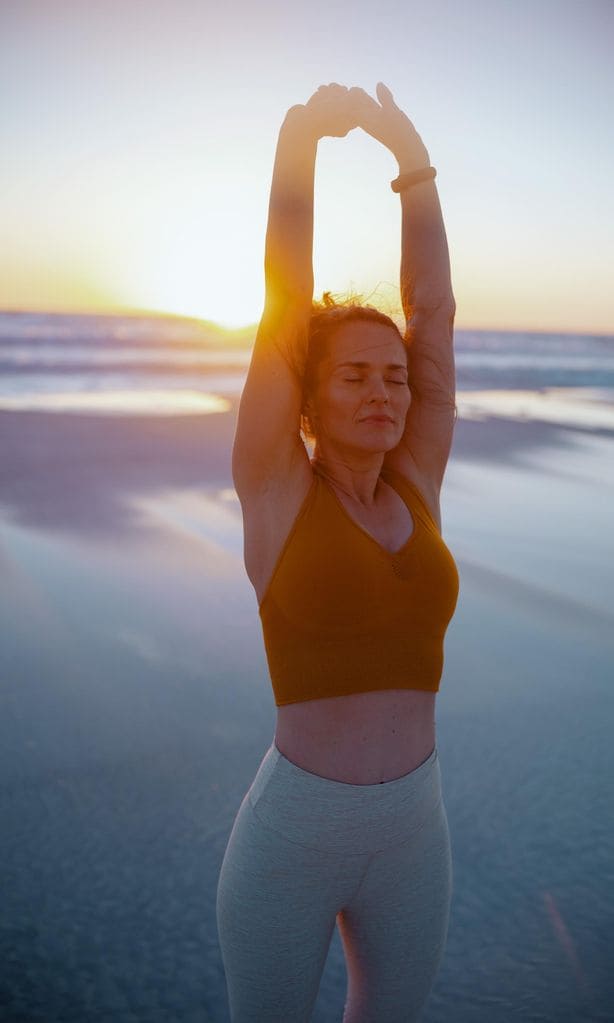 Mujer relajada practicando deporte en la playa con el atardecer