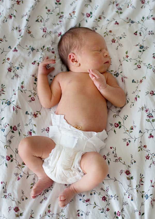 Bebé tumbado en una cama con colcha de estampado de flores