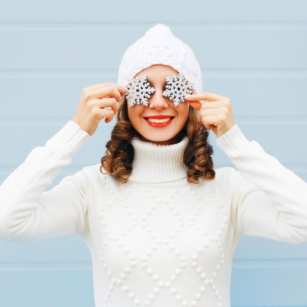 Mujer sonriente con un gorro de punto y suéter divirtiéndose con copos de nieve en la cara
