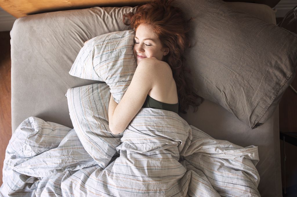 Mujer pelirroja durmiendo en su cama con una sonrisa