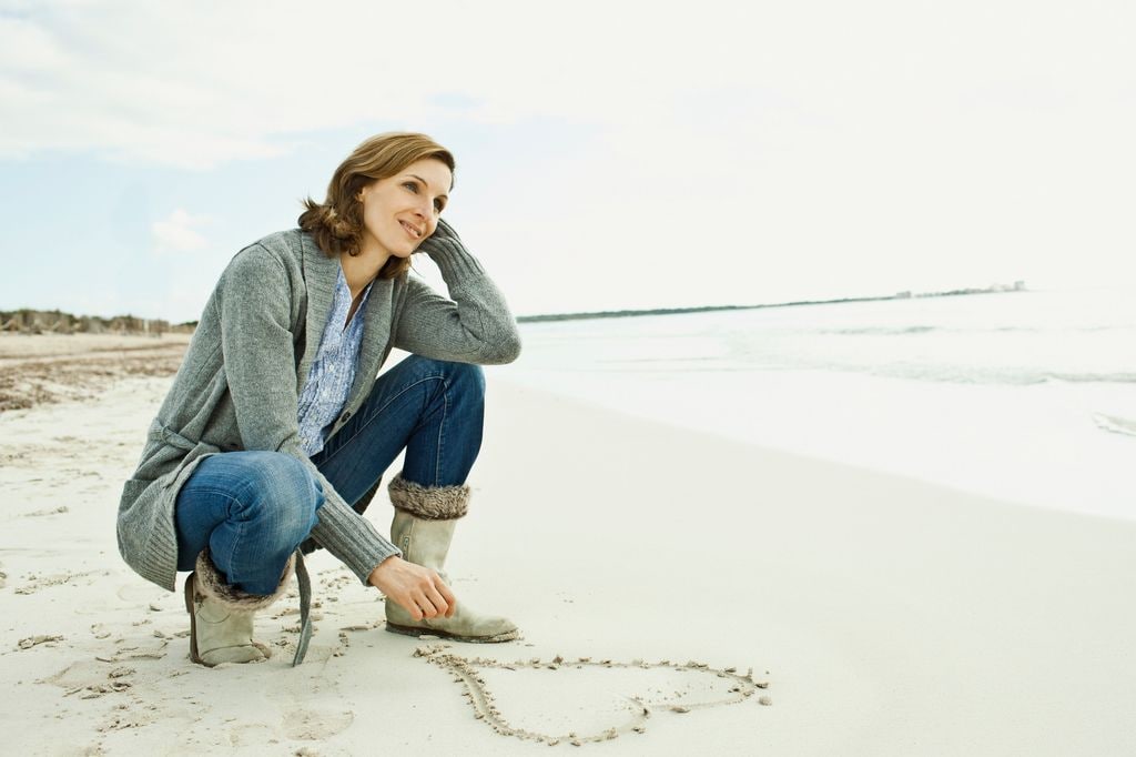 mujer en la playa, dibujando un corazón en la arena