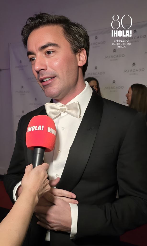 Fernando García, fashion designer, dressed in a black tuxedo and white bird, being interviewed on the red carpet of the Global Market Fashion Forward gala