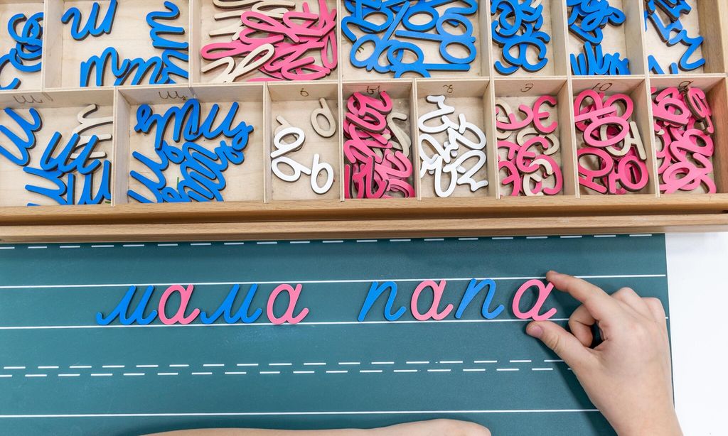 top view of kids hands building words by using colored montessori movable alphabet from the wooden tray on blackboard 