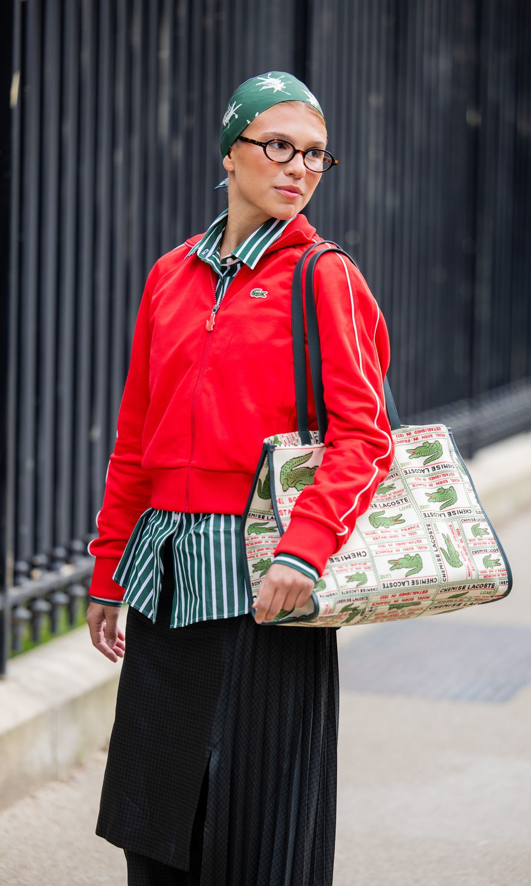 Rita Montezuma lleva un pañuelo verde en la cabeza, una camisa polo larga roja, una falda plisada negra, una blusa de rayas, un bolso y gafas. Esto ocurrió fuera de Lacoste durante la temporada de ropa femenina otoño/invierno 2025/2026, como parte de la Semana de la Moda de París, el 9 de marzo de 2025 en París, Francia.