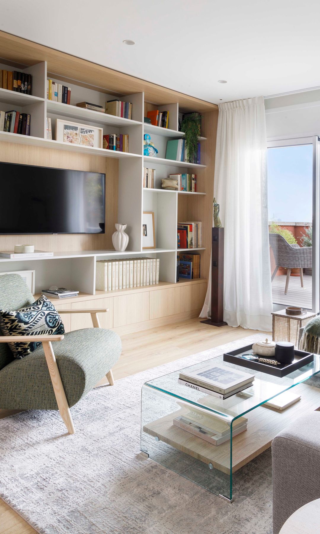 Salón con sofá gris, mesa de centro de cristal y librería a medida