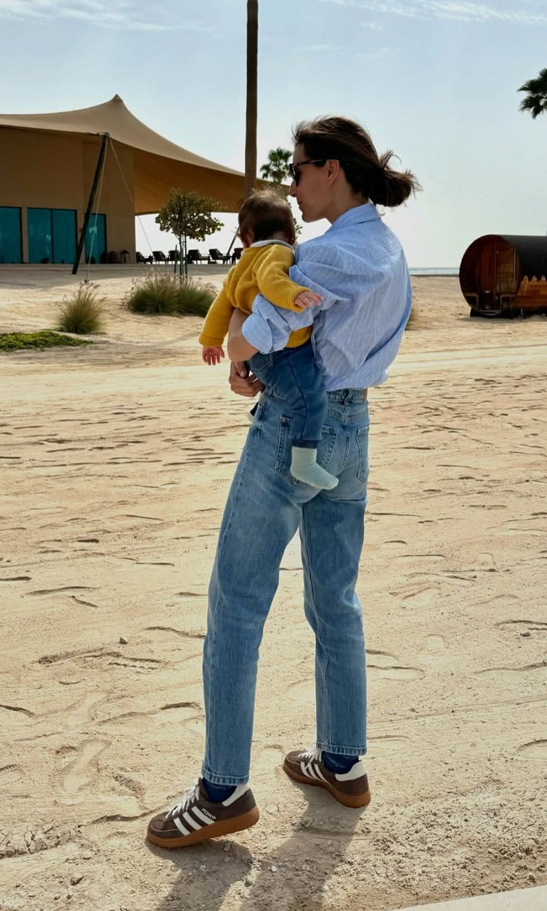 Ana Boyer con vaqueros, camisa de rayas y zapatillas de Adidas con su hijo en brazos en una playa