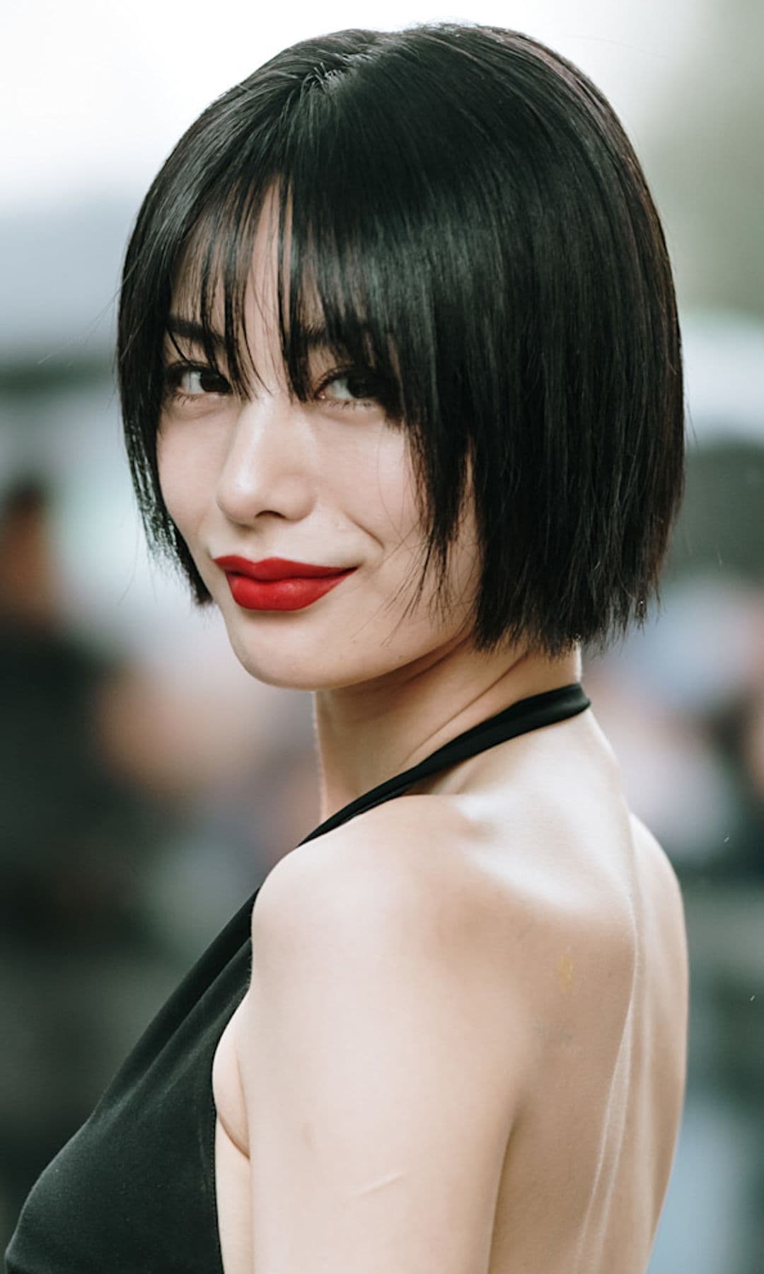 Brunette woman with black dress tied at the neck, red lips and short hair with bangs