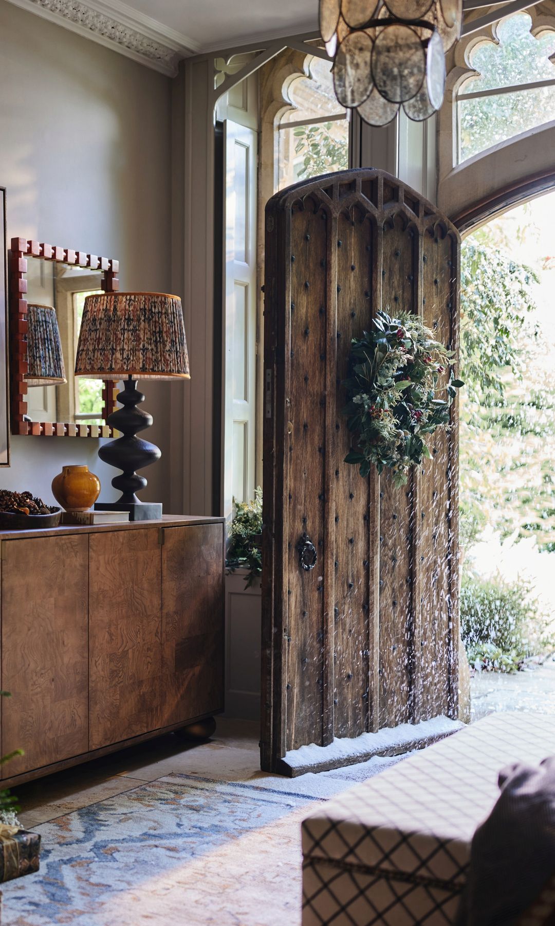 Entrada casa con puerta abierta con corona de Navidad, aparador, alfombra y árbol de Navidad 