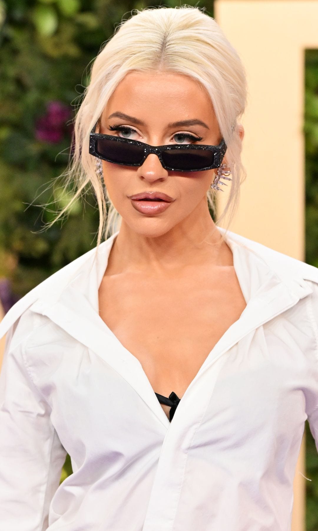 Christina Aguilera con camisa blanca abierta, falta plateada y gafas de sol en 2025