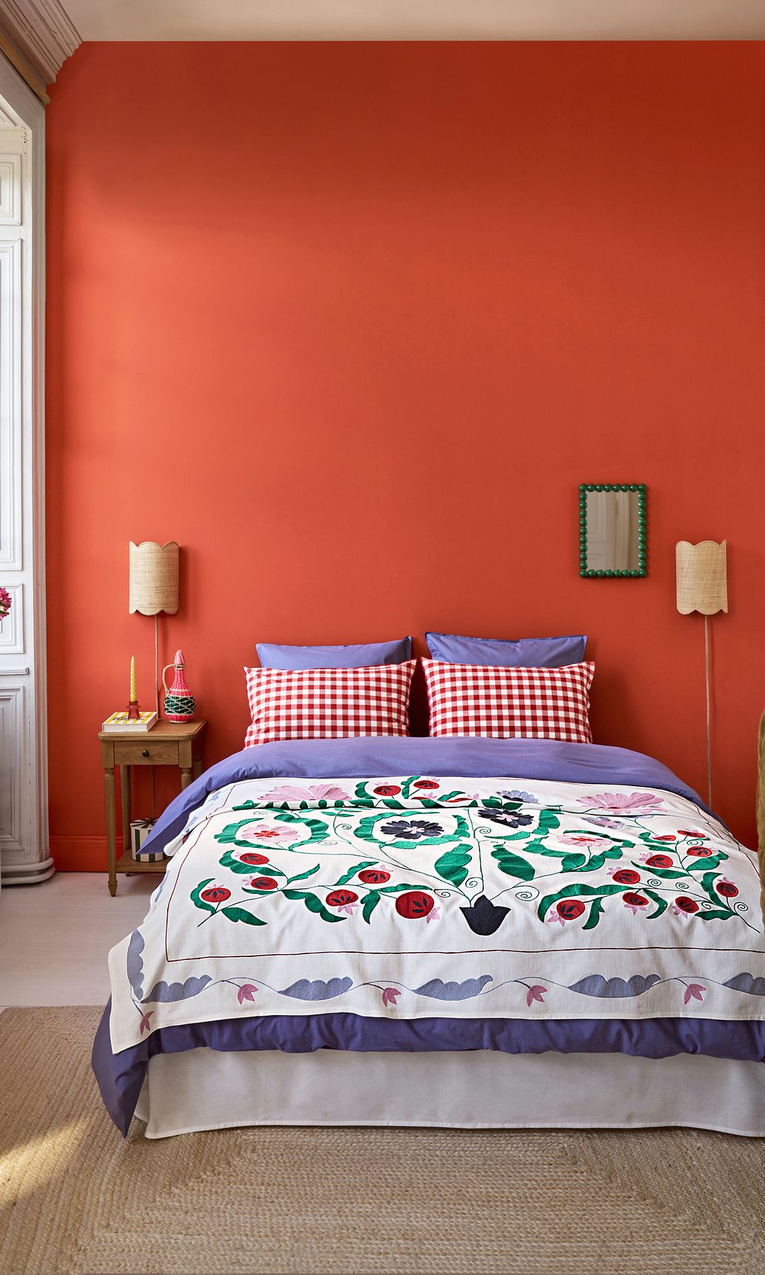 Dormitorio con pared naranja, ventana, repisa del radiador con jarrones, ropa de cama estampada 