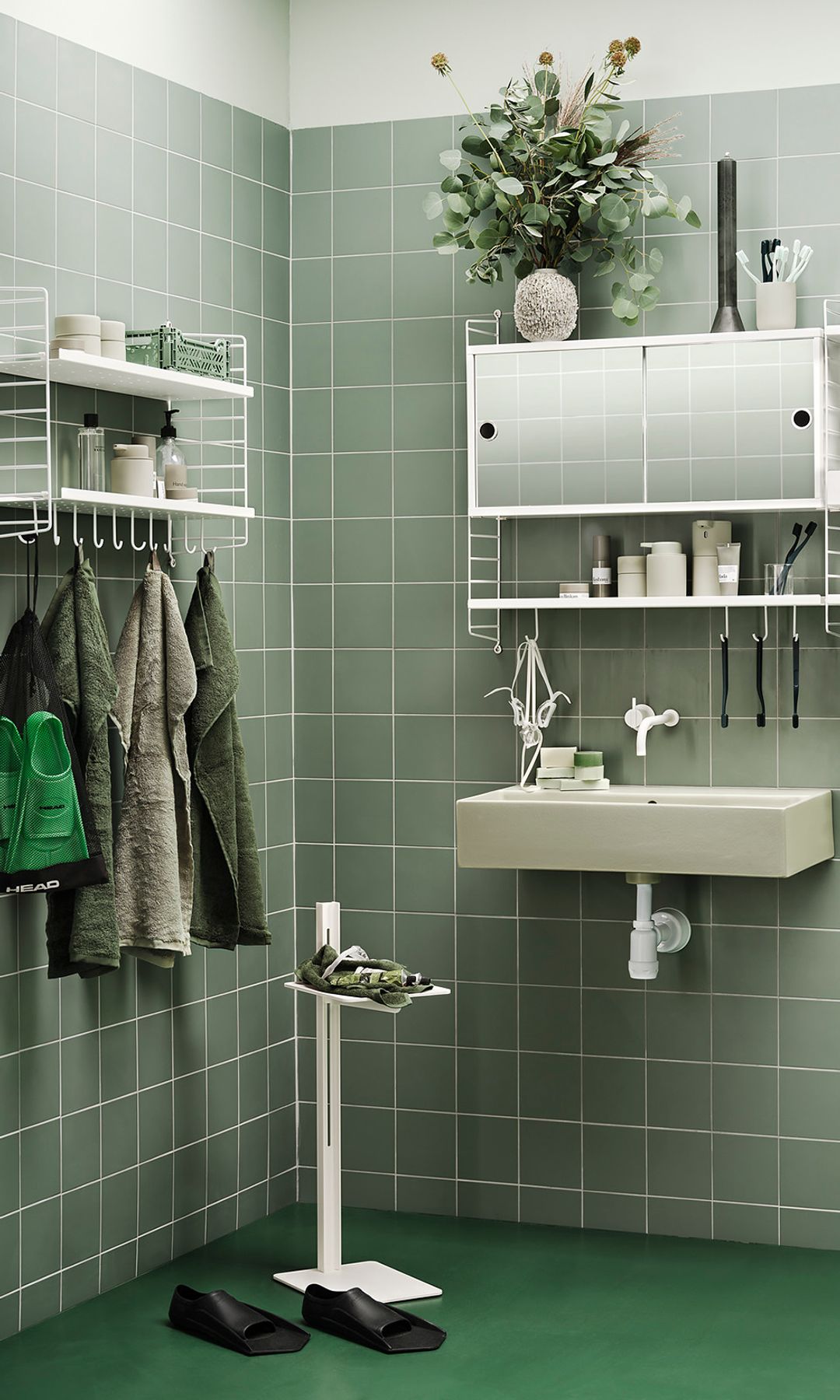 Baño con paredes de azulejos cuadrados verdes, suelo verde y estanterías metálicas blancas