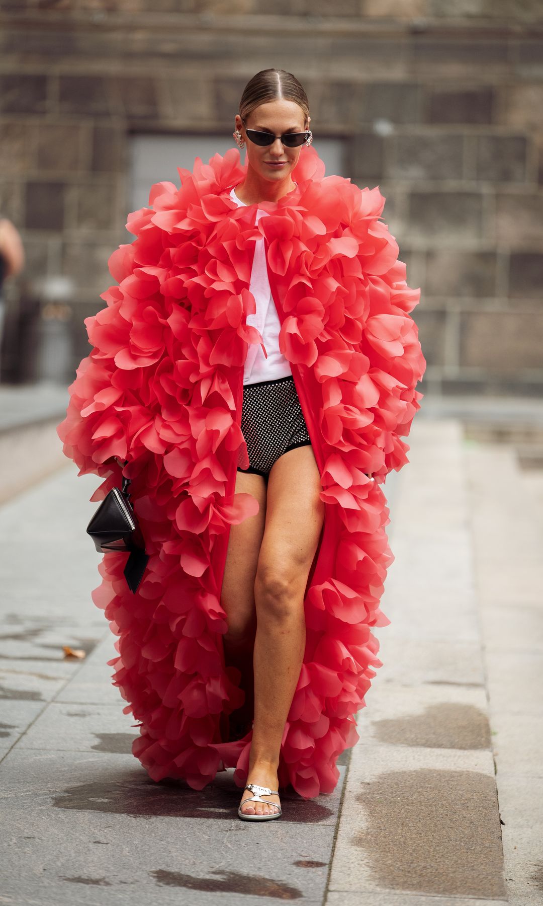 Tine Van Cauwenberghe lleva camiseta blanca, mini shorts brillantes, abrigo largo rojo de manga larga hecho de pétalos de flores rojas, gafas de sol y bolso negro fuera del desfile Rotate durante el cuarto día de la Copenhagen Fashion Week (CPHFW) SS25 el 08 de agosto 2024 en Copenhague, Dinamarca.