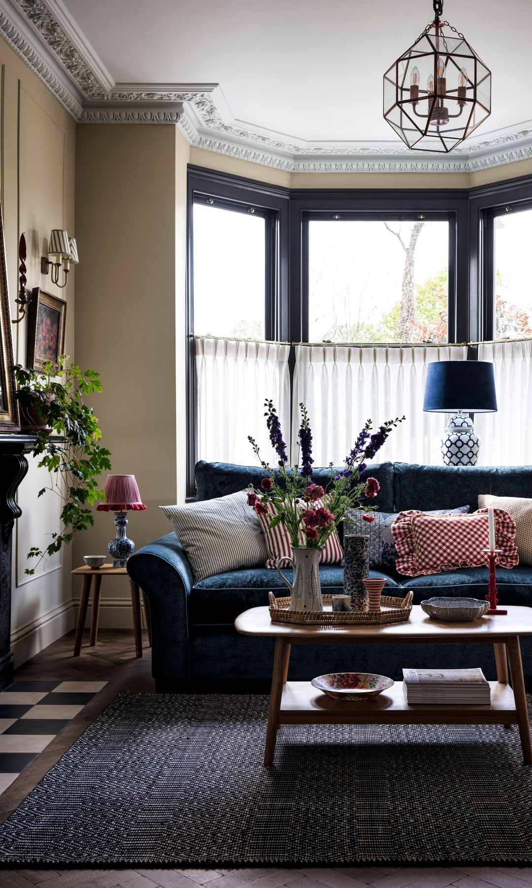 Salón con sofá de terciopelo azul, alfombra, mesa de centro de madera, chimenea, plantas y jarrón con flores