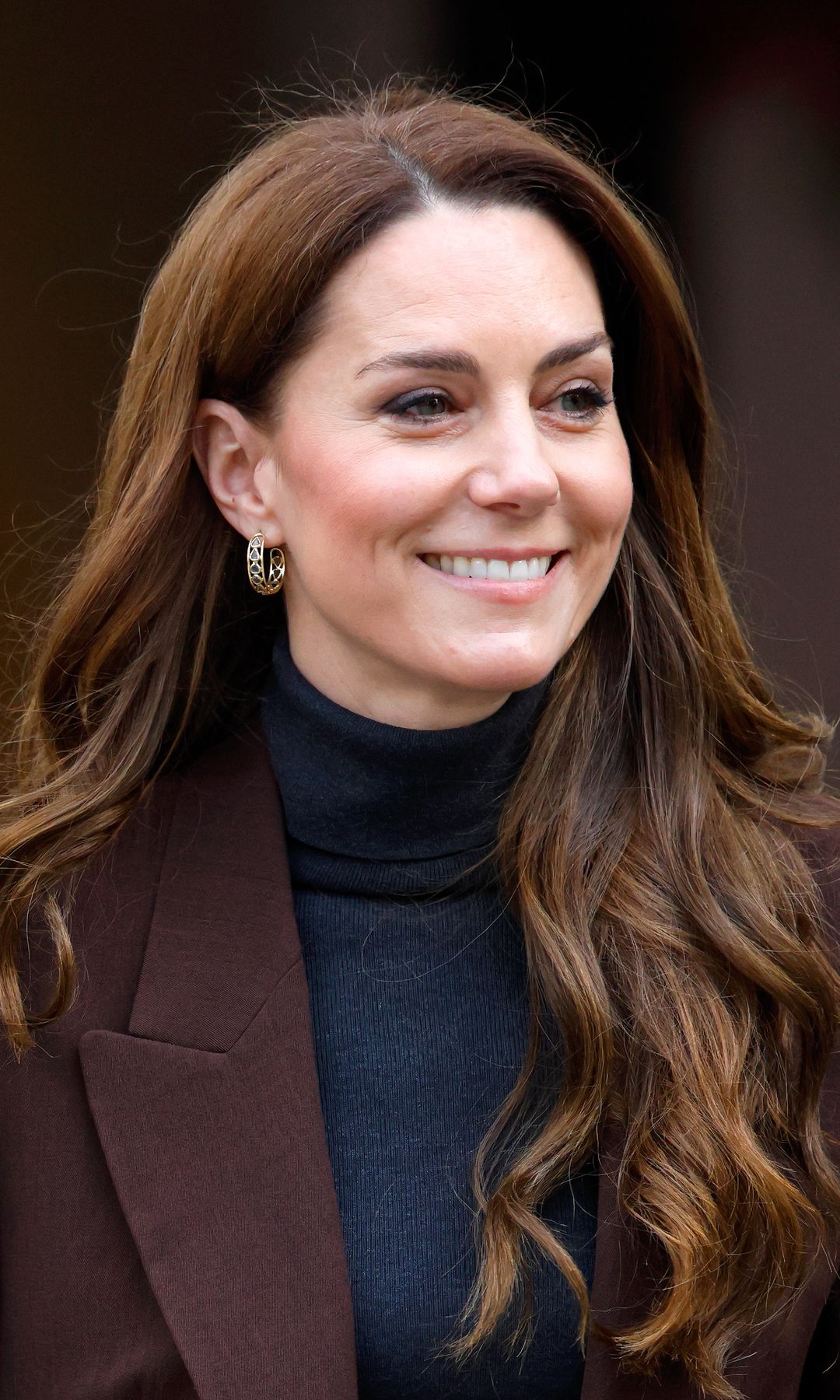 Kate Middleton con jersey de cuello alto, americana y pendientes de aro en Londres