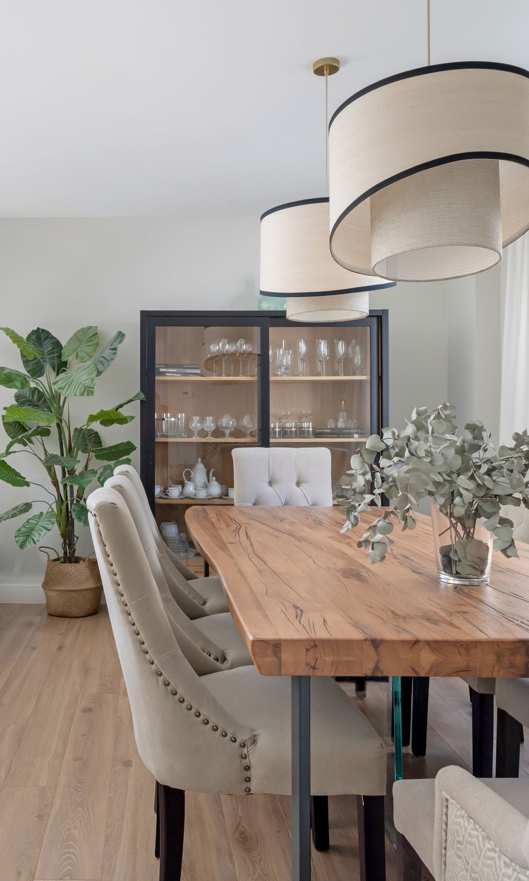 Comedor con mesa de madera, vitrina con el marco negro, sillas tapizadas y lámparas de suspensión