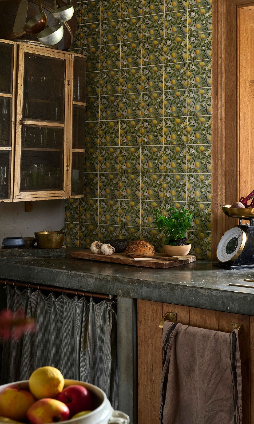 Cocina antigua con pared de azulejos amarillos y verdes, mueble de madera, cortinilla en la parte inferior y encimera oscura