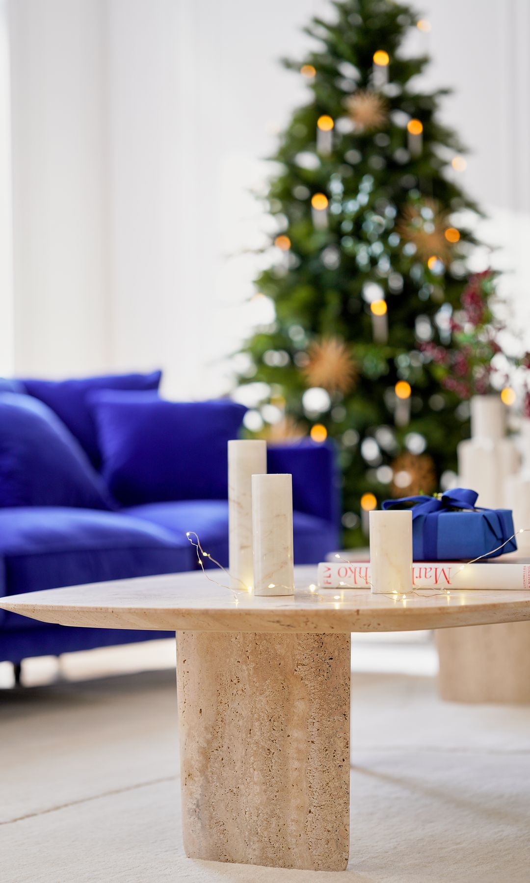 Salón con sofá azul, árbol de Navidad y mesa de centro de mármol con guirnalda de luces y velas