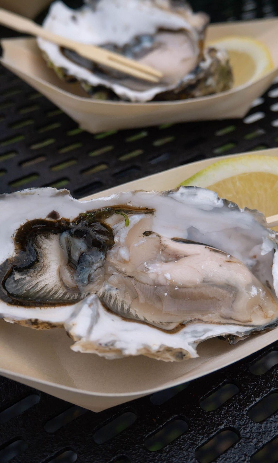 Ostra cruda fresca en su concha nacarada con limón en un plato de papel sobre una mesa de hierro negro