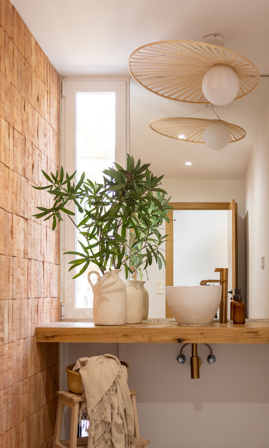 Baño con pared de azulejos rústicos, lámpara de fibras, encimera de madera, planta y taburete