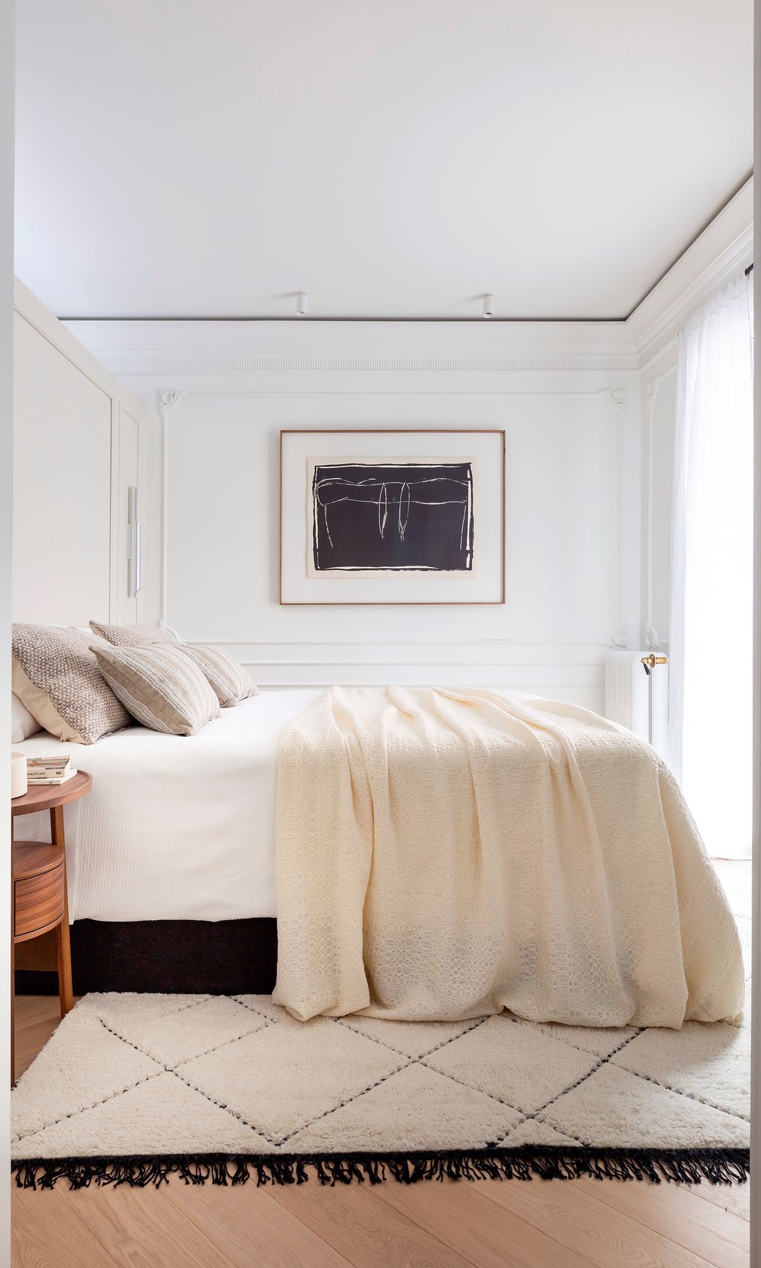 Dormitorio blanco con alfombra con flecos negros y cuadro en la pared