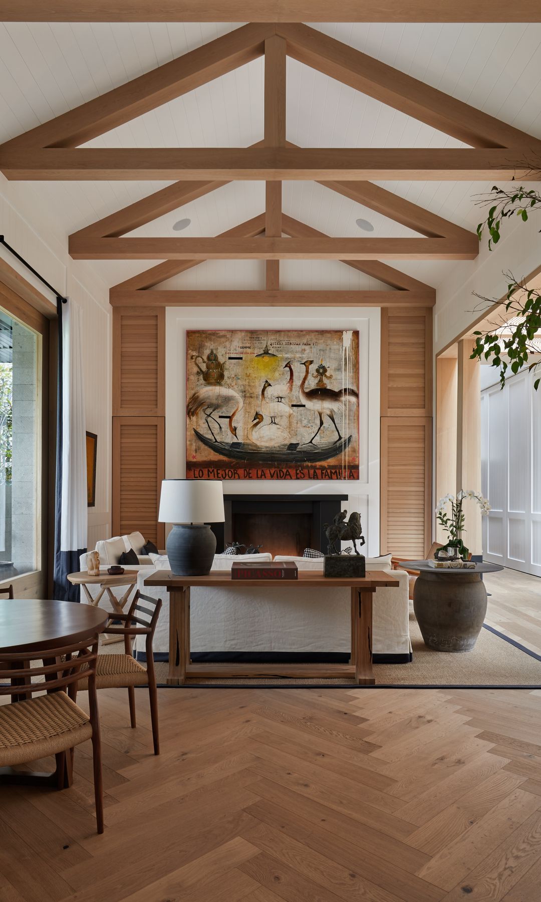 Salón comedor con chimenea, suelo de madera, vigas de madera en el techo, cuadro y sofá blanco 