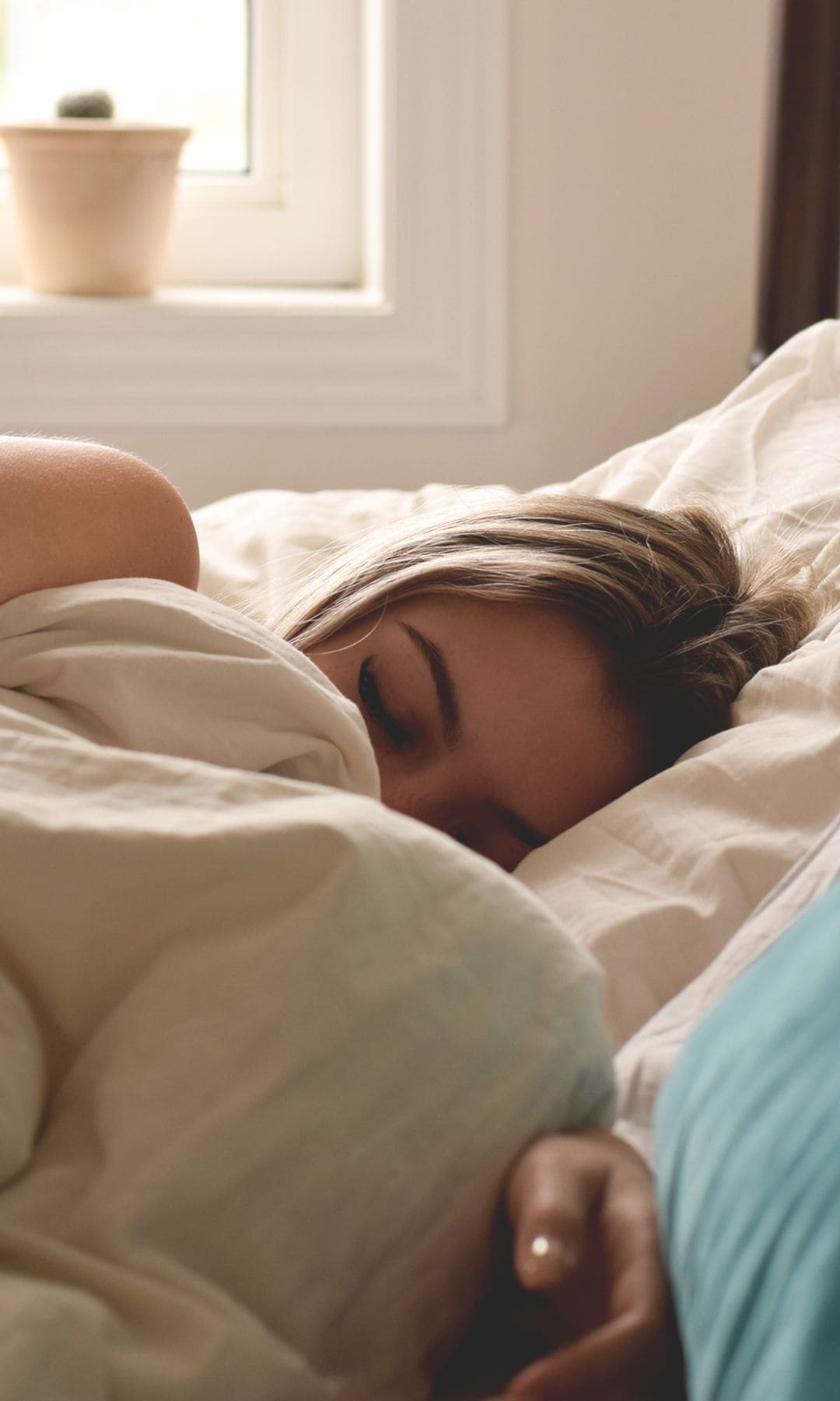 Mujer durmiendo en la cama con sábanas blancas y muy tapada con su funda nórdica