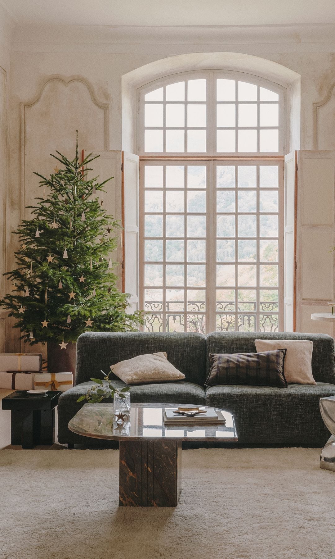 Salón con árbol de Navidad, sofá verde, mesa de centro mármol, paredes con textura, mesa auxiliar cromo