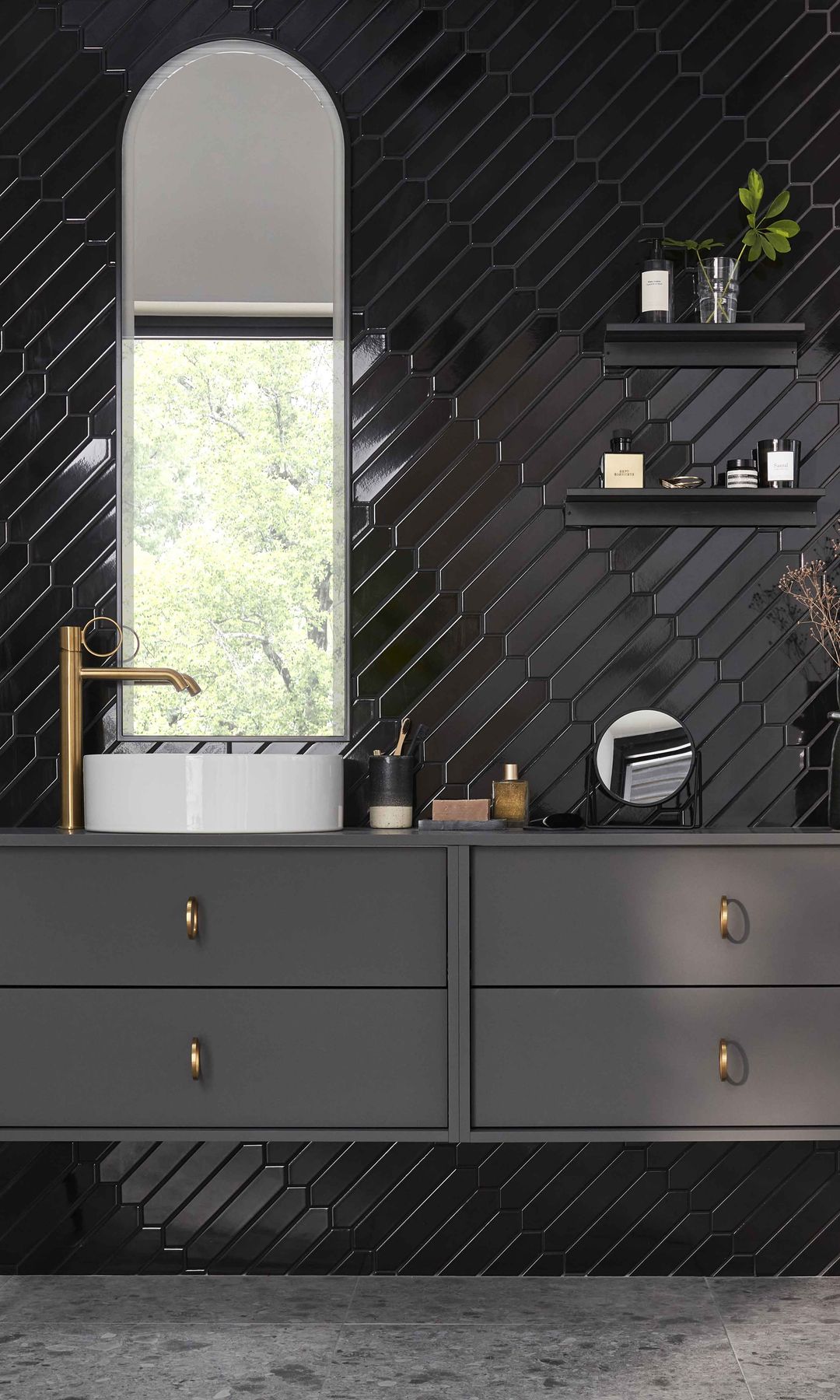 Baño negro con azulejos brillantes, mueble bajolavabo suspendido gris, espejo ovalado y grifería dorada