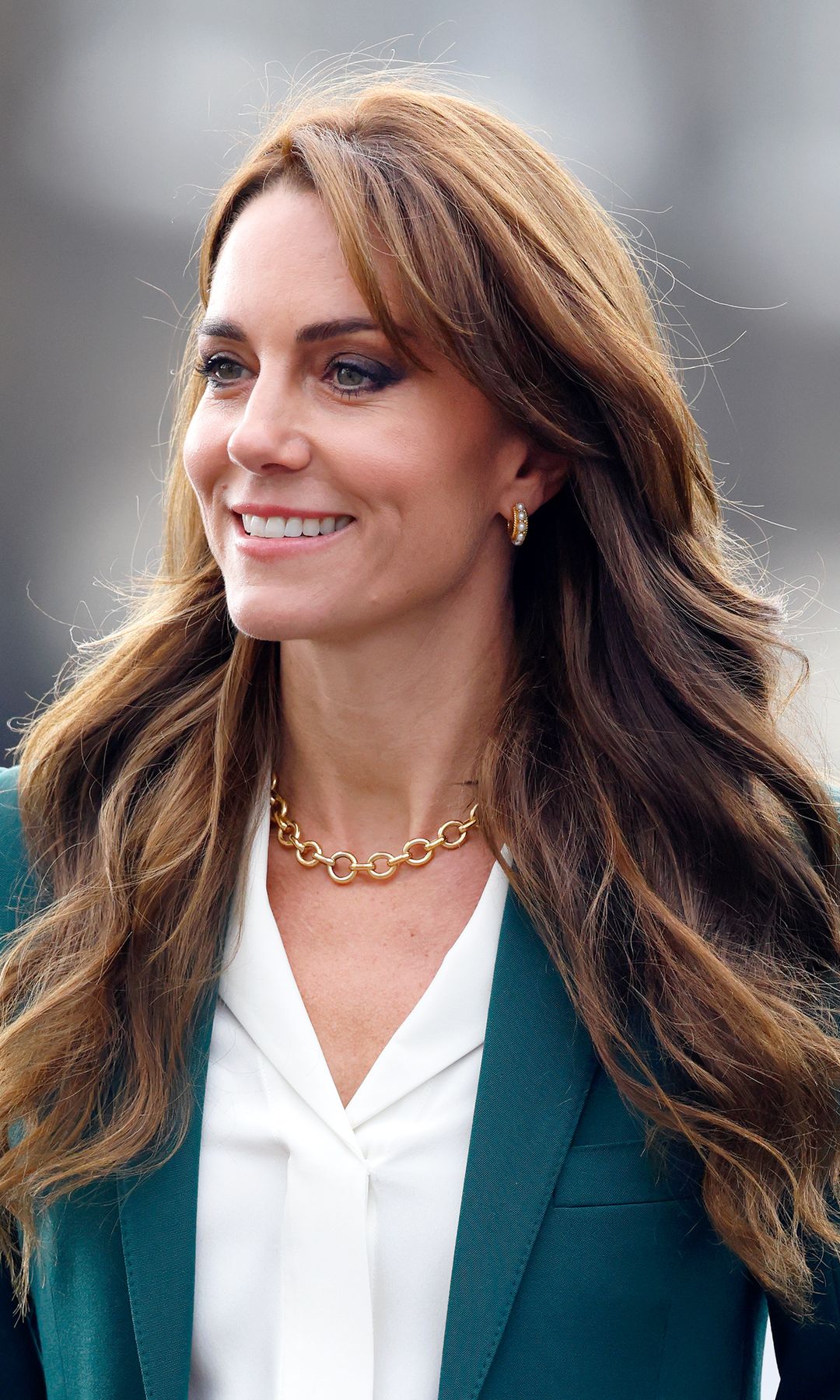 Kate Middleton con camisa blanca, americana azul, collar de cadena y pendientes de aro con perlas