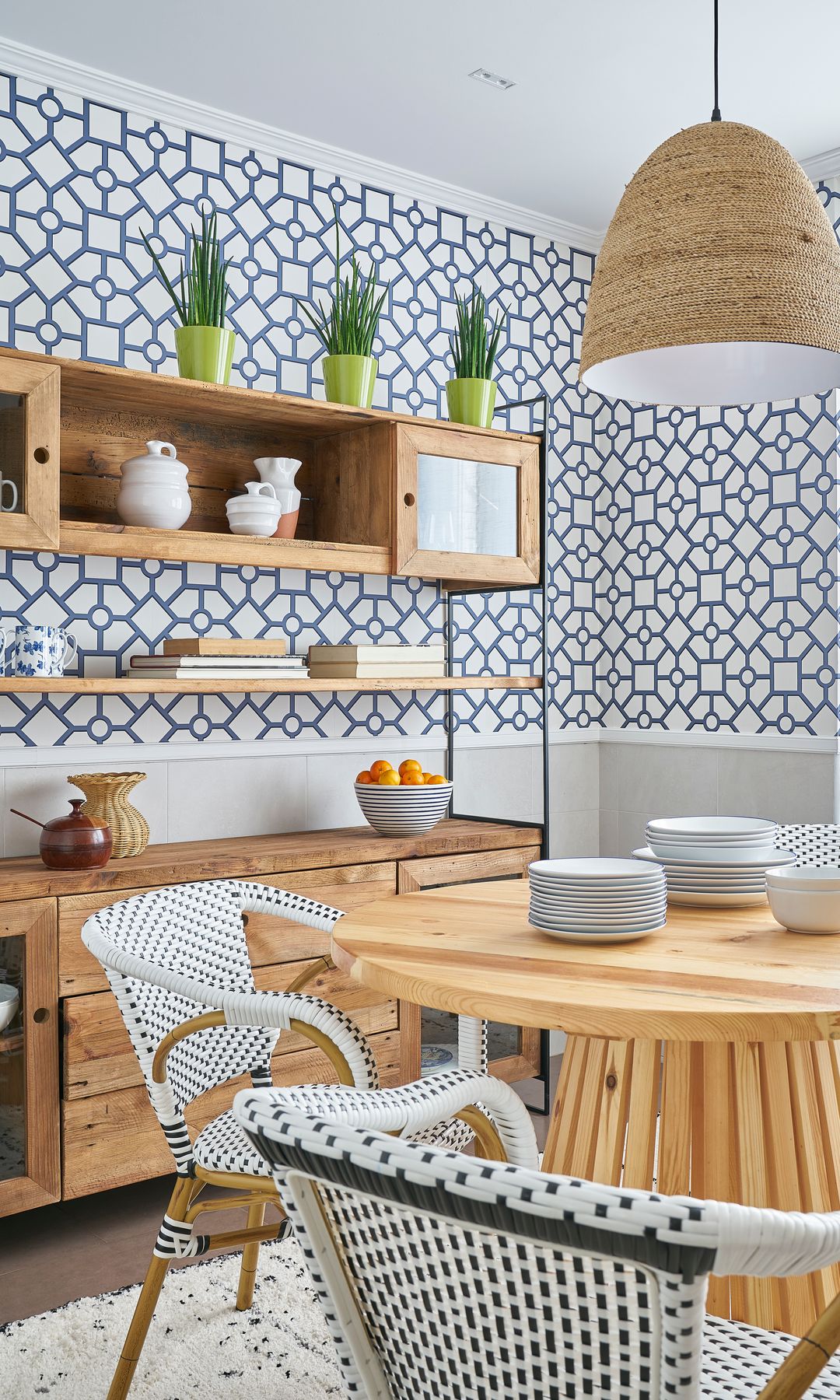 Office con mesa de madera, papel pintado con motivos geométricos blancos y grises, aparador de madera, lámpara de techo de fibras y estantería con puertas de cristal