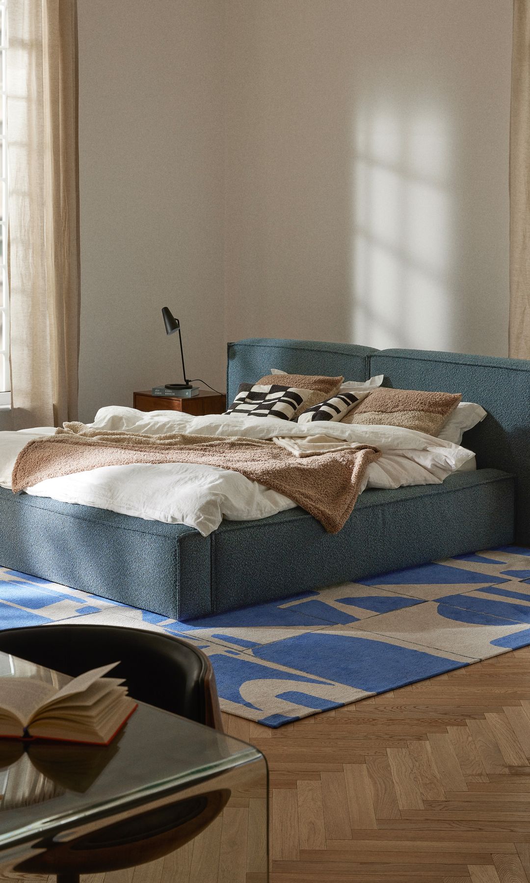 Dormitorio con cama tapizada azul, alfombra azul y crema, gran ventanal 