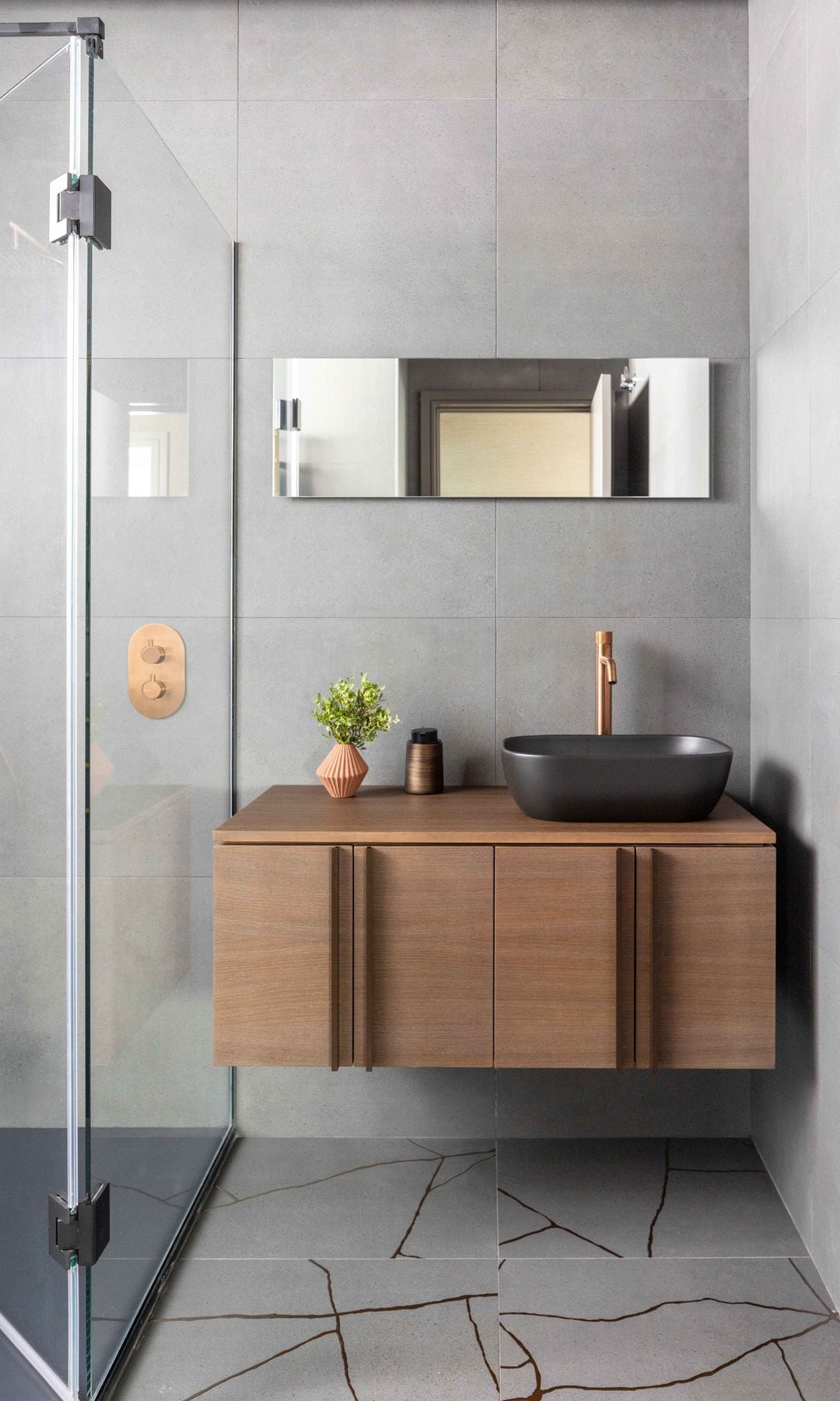 Baño con ducha, mampara, suelo cerámico, mueble de madera, espejo y lavabo negro