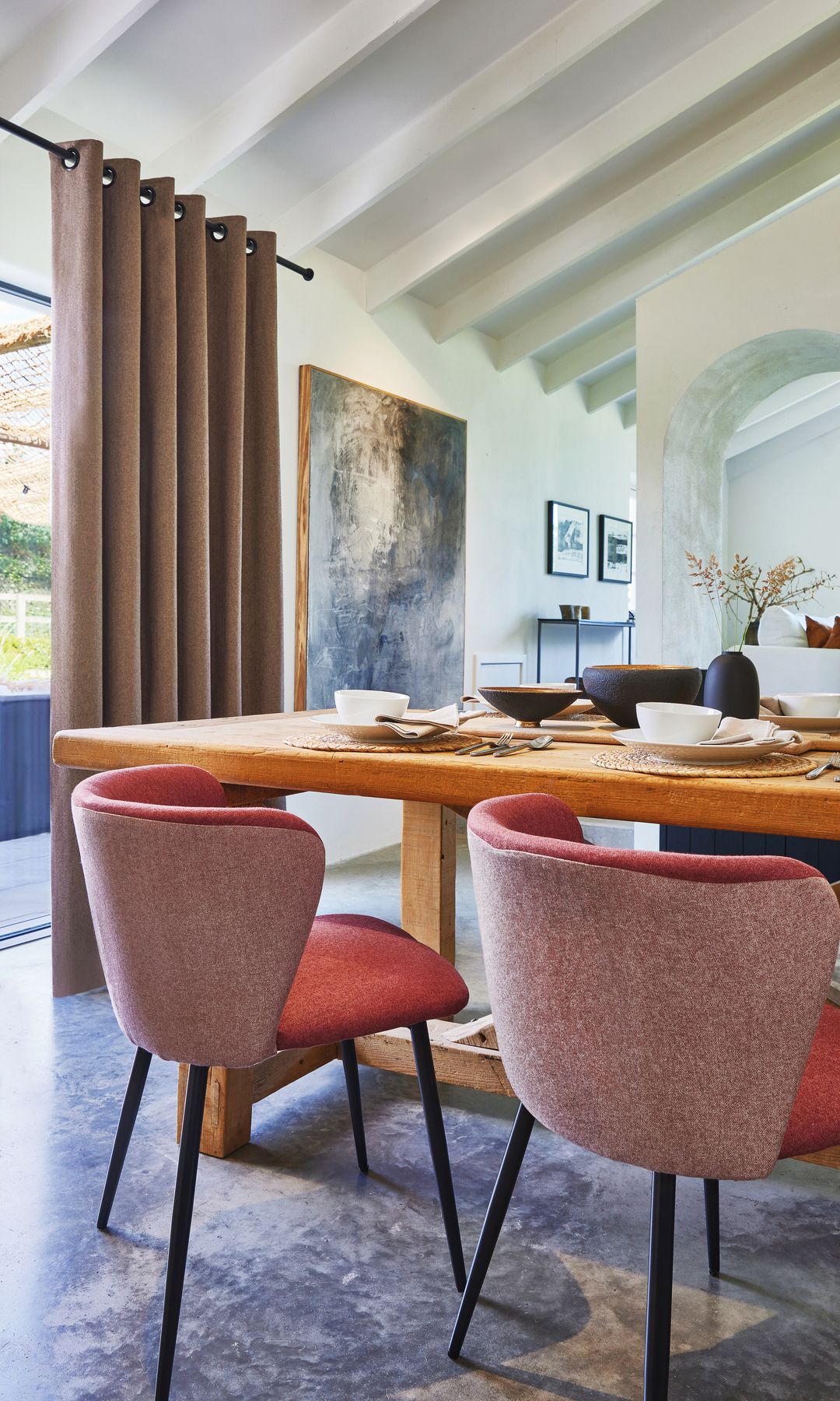 Salón comedor con cortinas marrones, mesa de madera, sillas tapizadas en rojo, bóveda catalana en el techo y arco