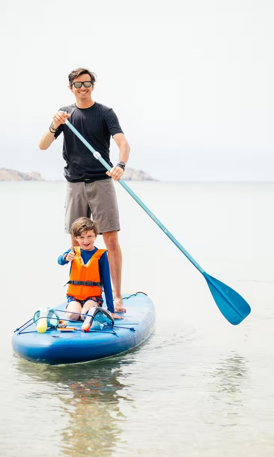 Padre e hijo practicando 'paddle surf' en la playa con tabla y chaleco