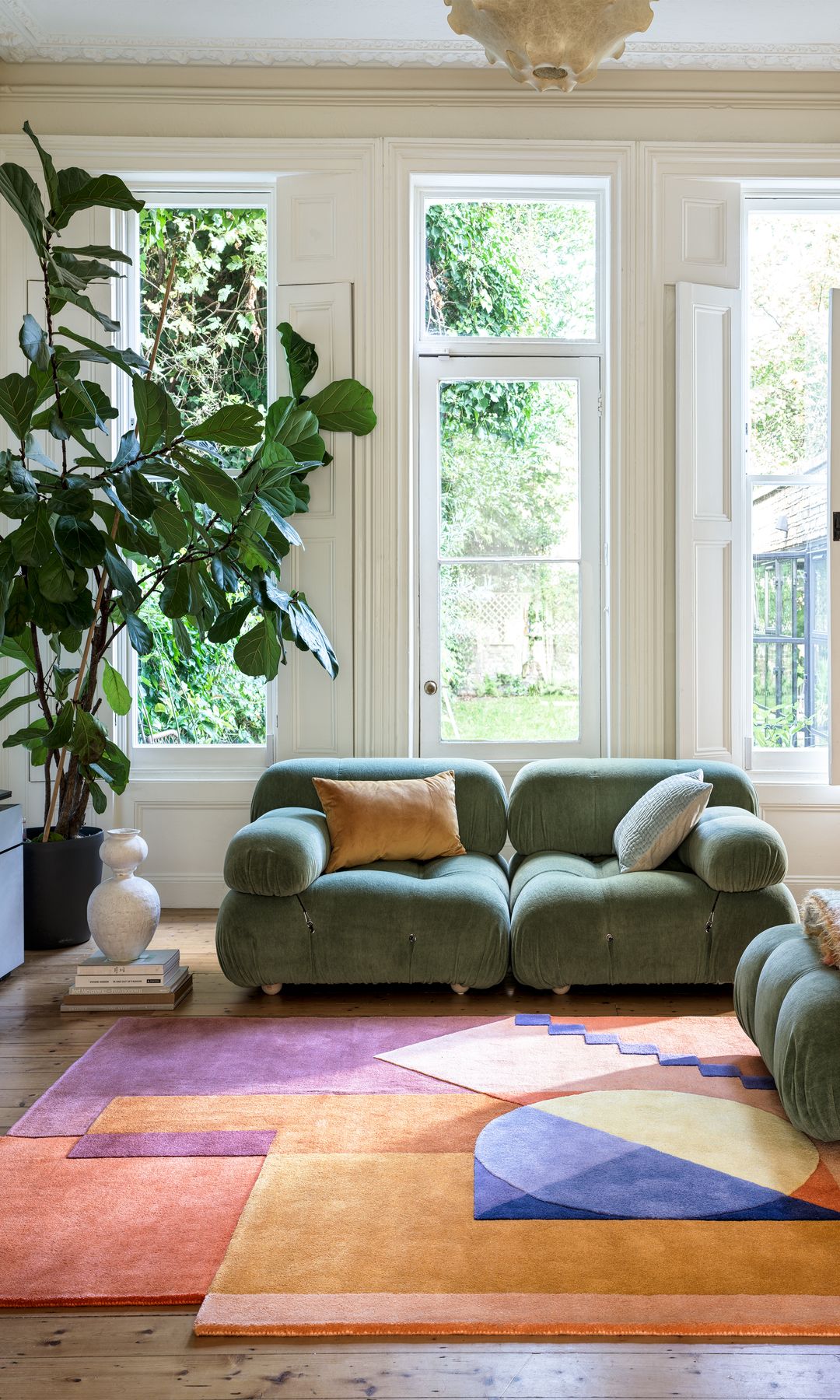 Salón con chimenea, alfombra asimétrica de colores, sofás verdes y una gran planta 