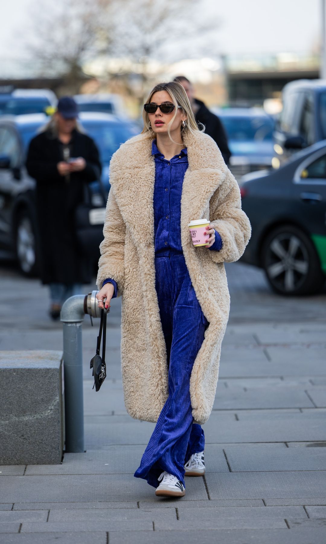 Una invitada lleva abrigo de peluche beige, pantalones de terciopelo azul, camisa de botones fuera de TG Botanical durante la Semana de la Moda de Copenhague AW24 el 01 de febrero 2024 en Copenhague, Dinamarca.