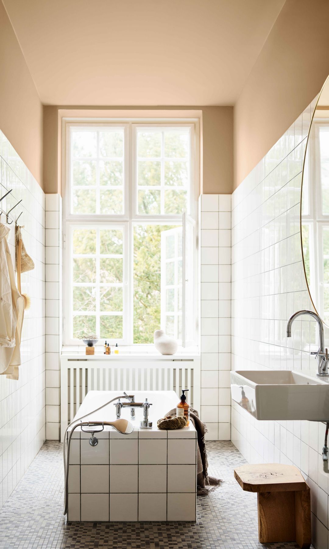 Baño con bañera y pared de azulejos blancos, suelo terrazo y pared melocotón