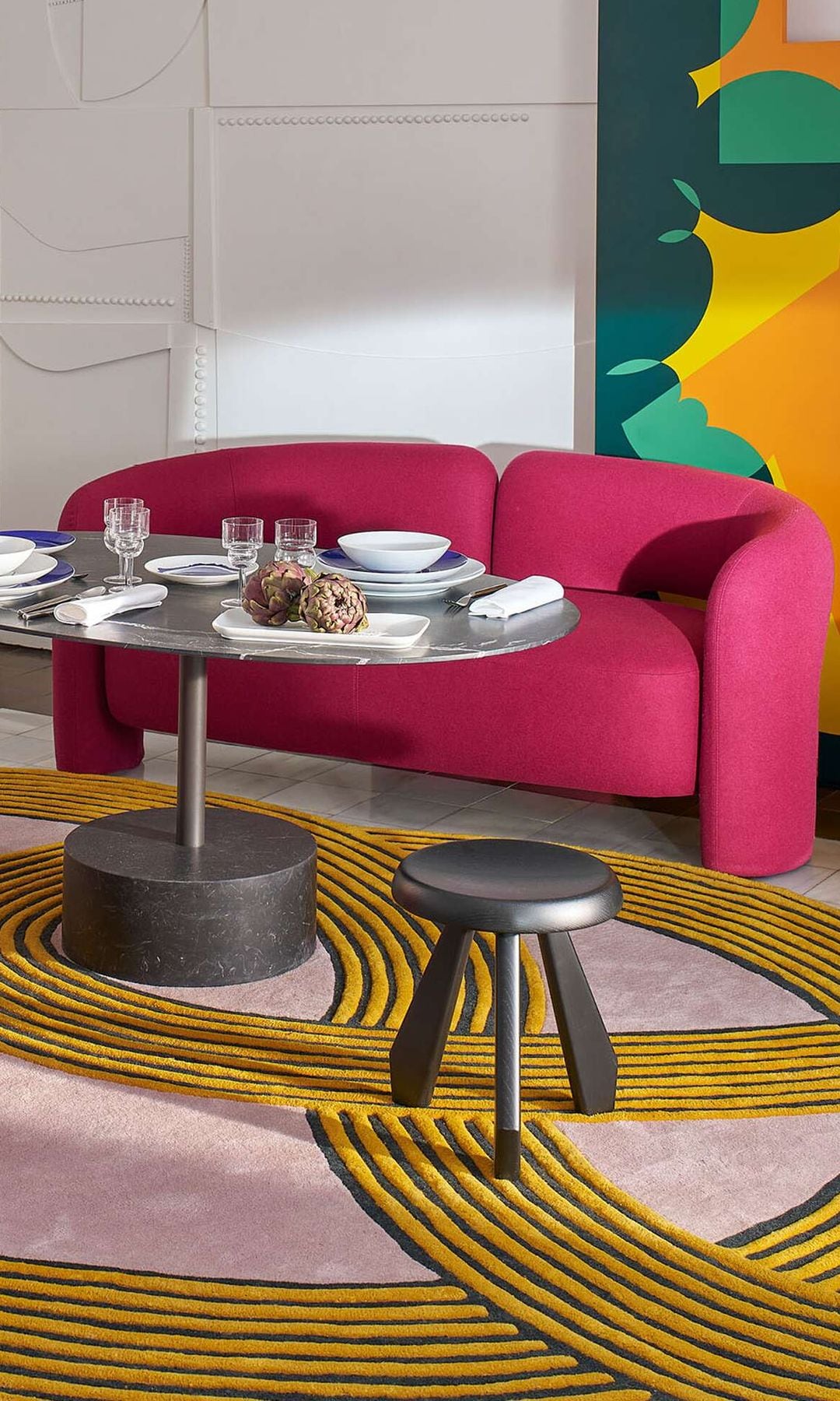 Salón con alfombra geométrica rosa y amarilla, sofás fucsias y mesa de centro y auxiliar metalizadas