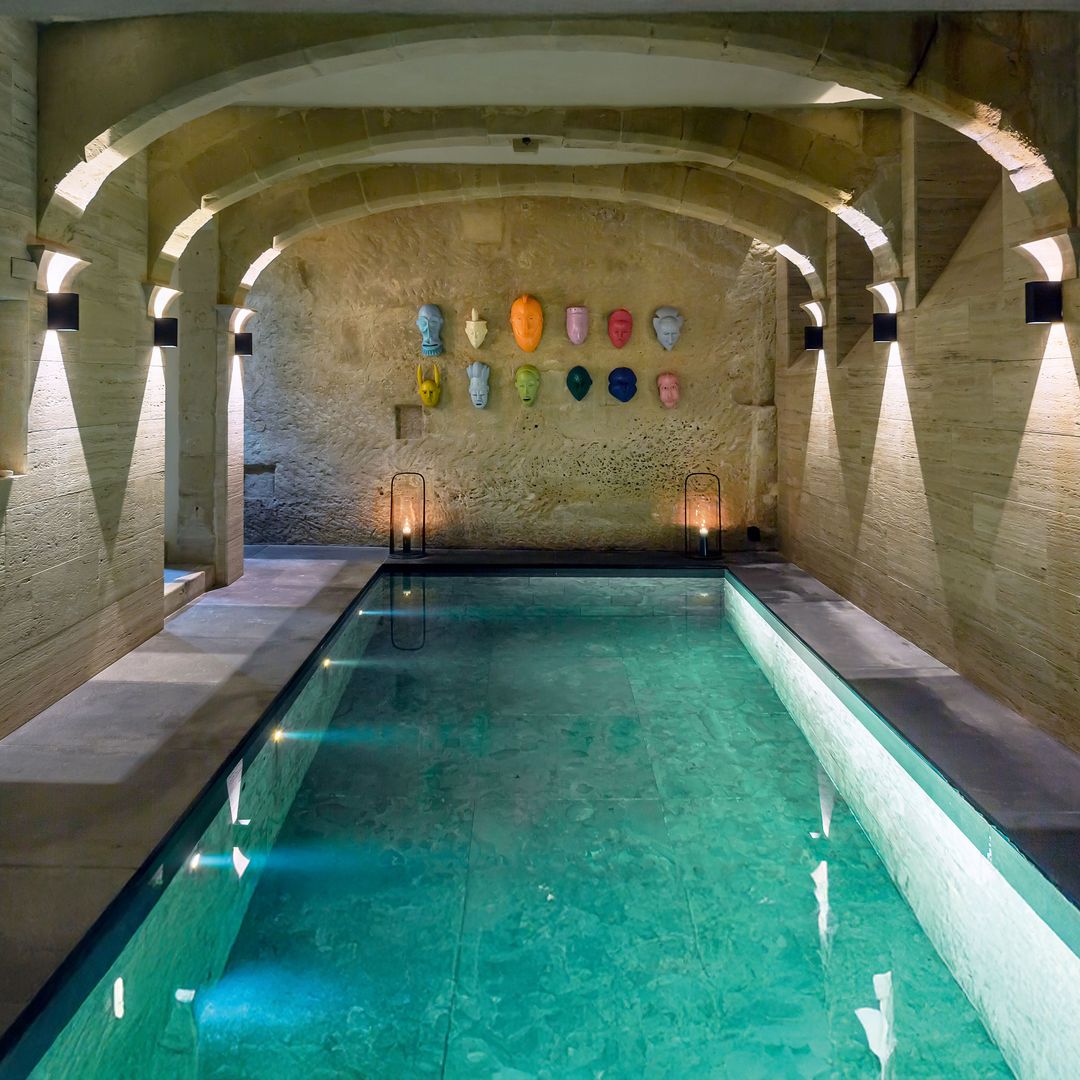 La piscina, que se encuentra en el sótano, bajo un arco de piedra caliza. En la pared, hay unas máscaras de Djordje Ozbolt y las lámparas de suelo son de Francis Sultana.