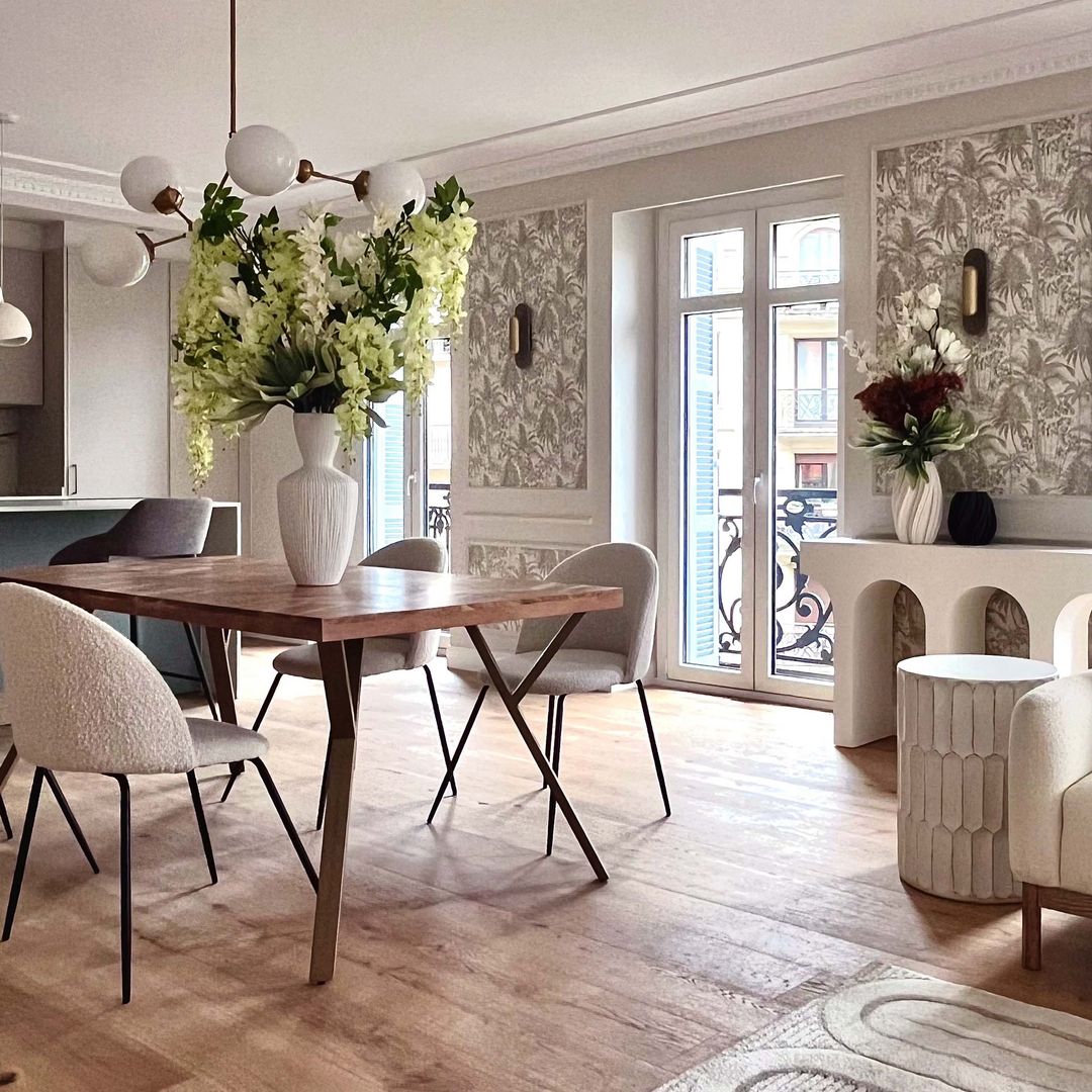 Salón comedor con suelo de roble, mesa de madera, sillas tapizadas, jarrón alto con flores, consola blanca, molduras y papel pintado