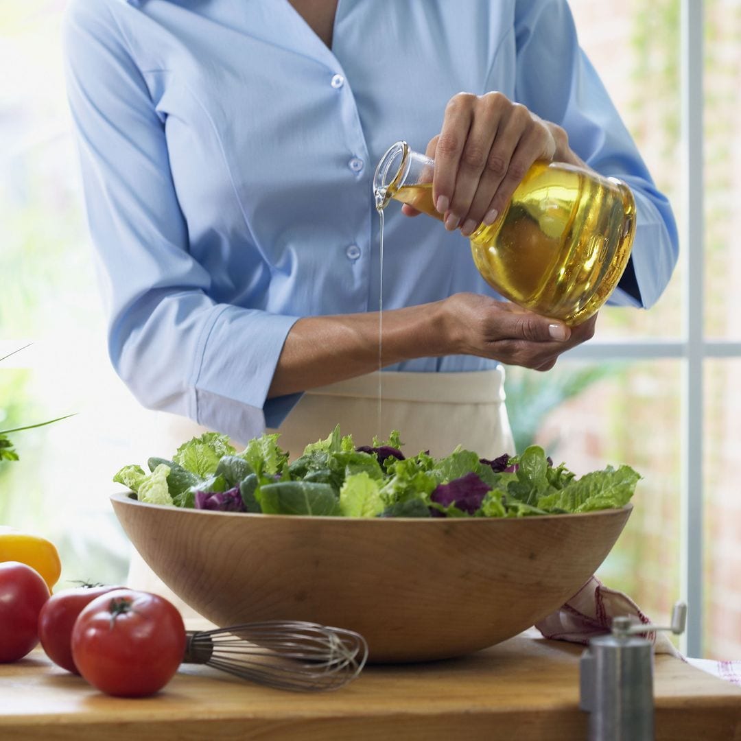 Mujer aliñando ensalada con aceite de oliva