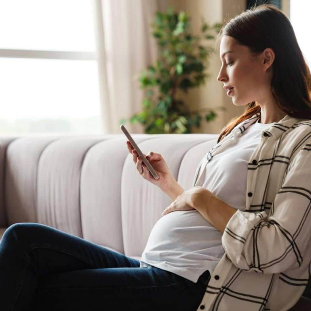 mujer embarazada con movil en la mano sentada en un sof 