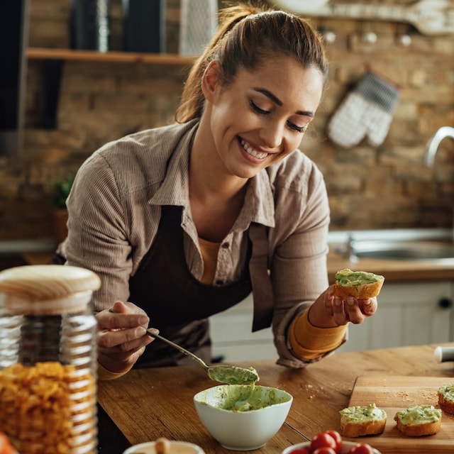 mujer sonriente preparando tostadas de aguacate en la cocina