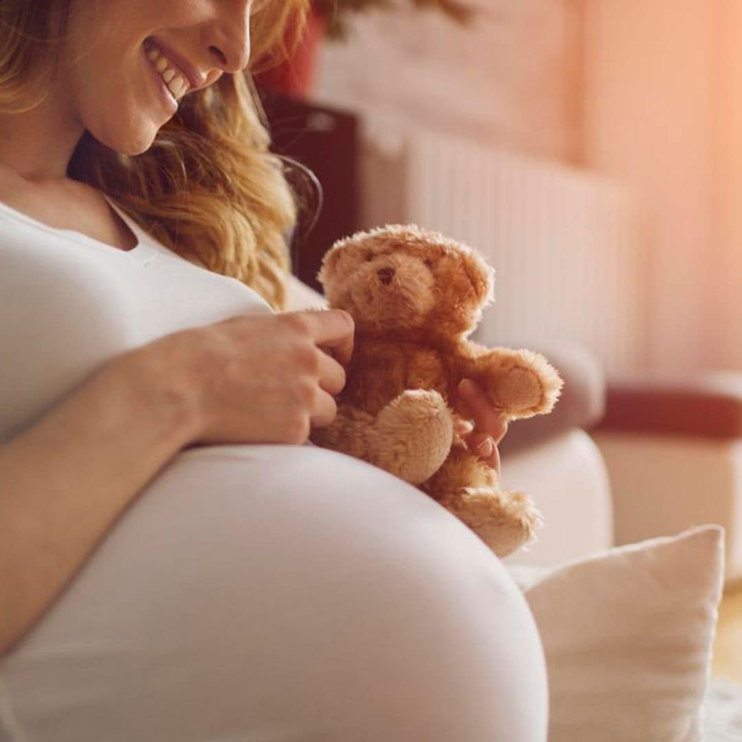 mujer embarazada con oso de peluche y sonriente