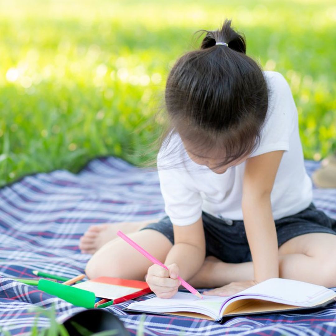 ni a con un cuaderno de verano en el c sped 