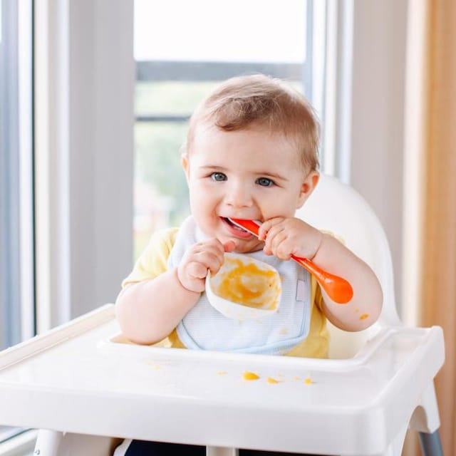 ni o comiendo solito papilla sentado en una trona