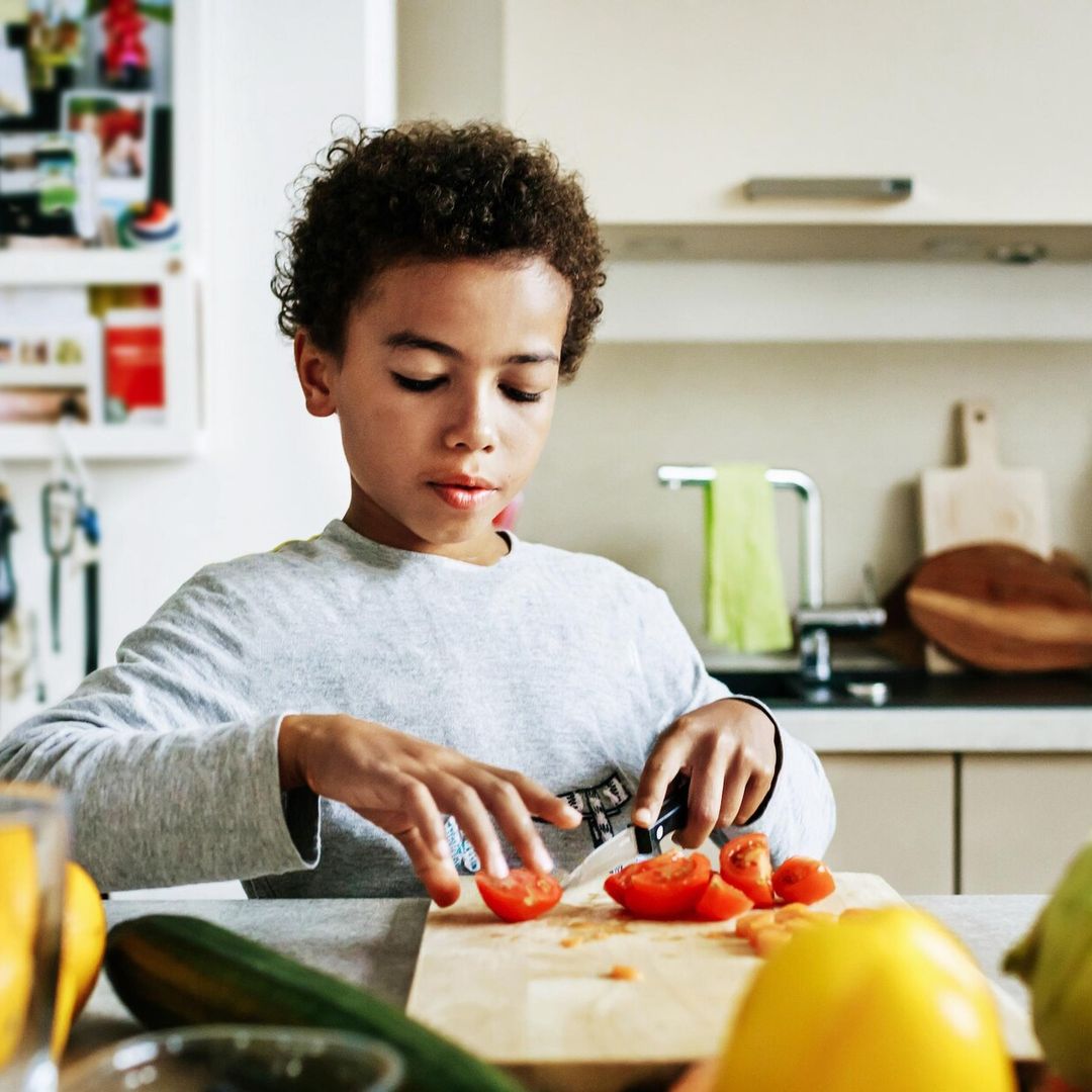 a young boy at home helping his dad to prepare lunch by slicing some tomatoes 